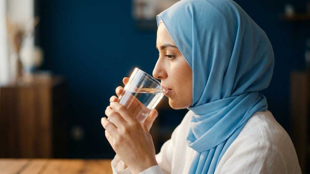 Water in Islam Muslim woman sipping water from glass side profile