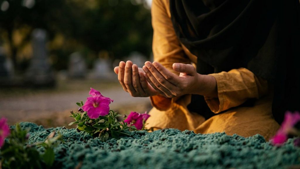Close view of a Muslim woman's hands and the simple earth mound during the Dua After Burial.