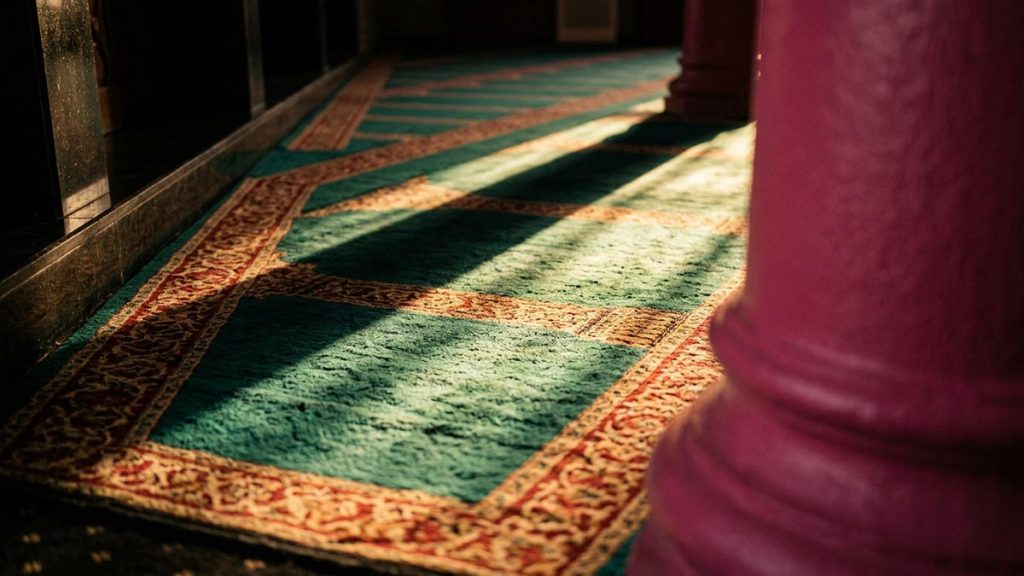 A still-life of long afternoon shadows falling across a prayer hall carpet, illustrating the Dua Before Asr.
