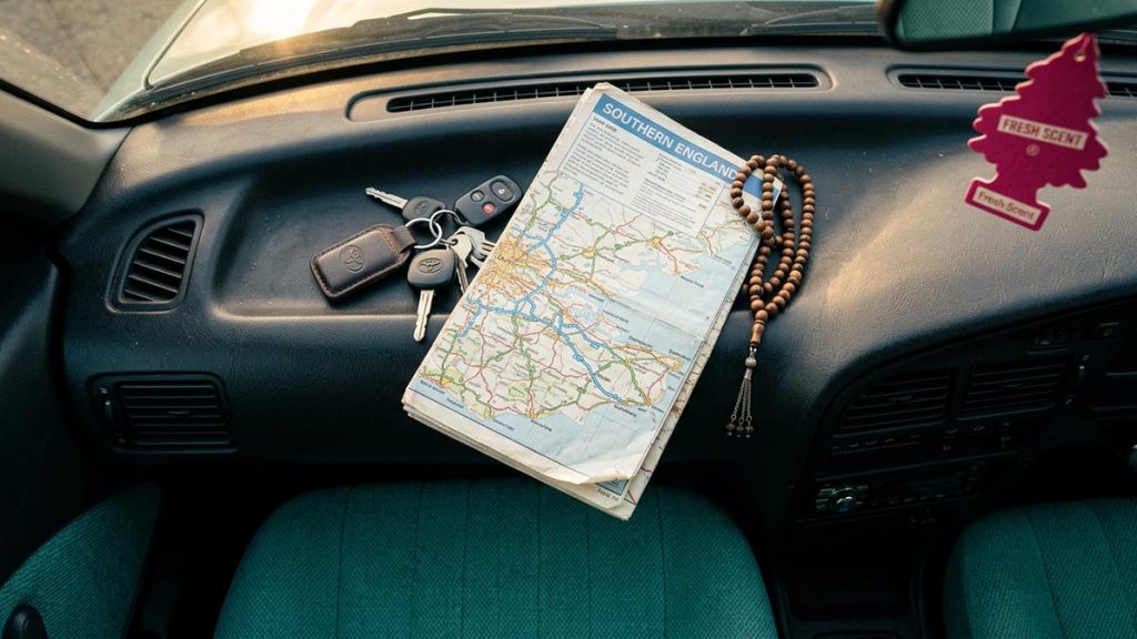 A still-life of car keys, a folded road map and prayer beads on a car dashboard, illustrating the Dua Before Driving.