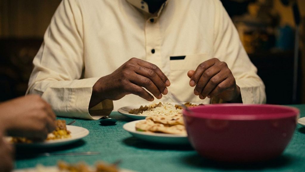 Close view of a Muslim man's hands and the plate of rice and bread during the Dua Before Eating.
