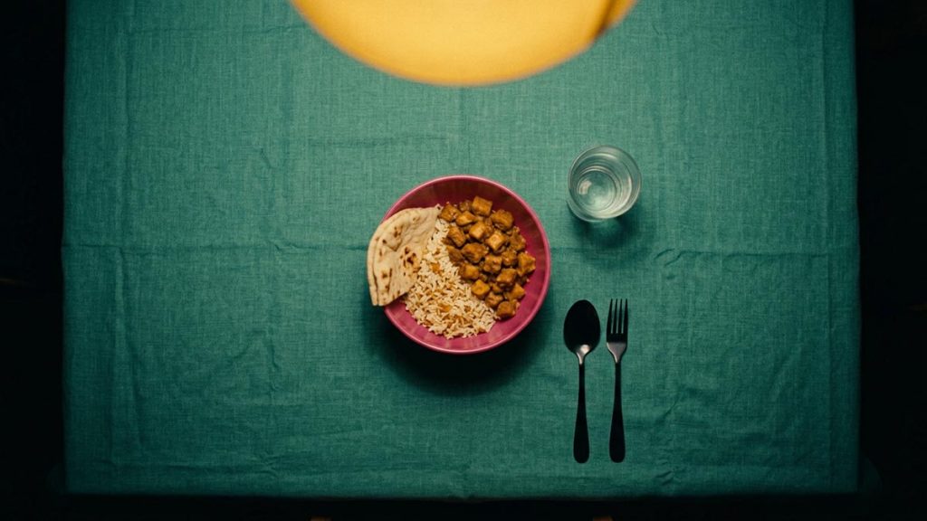 A still-life of a plate of rice and bread, a glass of water and a spoon laid on a table, illustrating the Dua Before Eating.