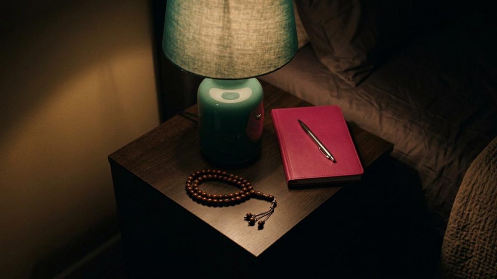 A still-life of a switched-off lamp, a closed notebook and prayer beads at bedside, illustrating the Dua Before Ending the Day.