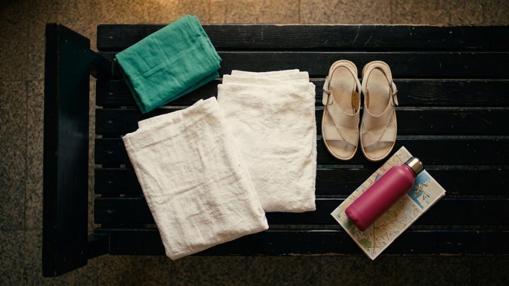 A still-life of folded white pilgrim garments, sandals and a water flask laid ready, illustrating the Dua Before Entering Ihram.