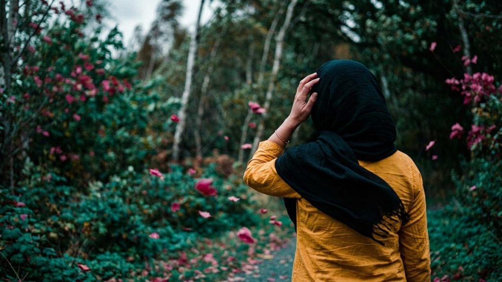 A Muslim woman seen from behind on a path where a strong wind is blowing, reflecting the Dua During Strong Winds.