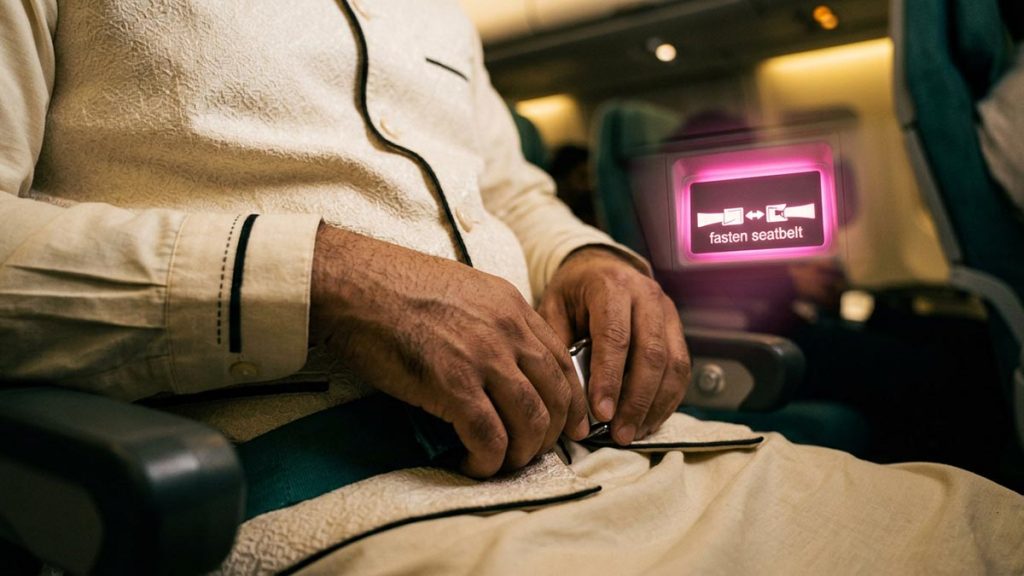 Close view of a Muslim man's hands and the fastened seatbelt and an illuminated seatbelt sign during the Dua During Turbulence.