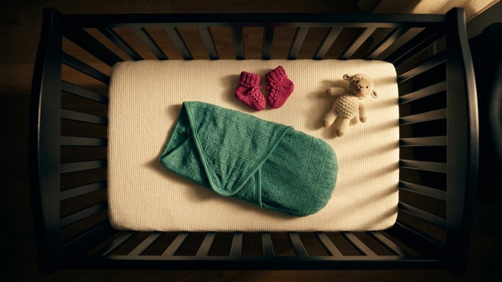 A still-life of a swaddled blanket, tiny knitted booties and a soft toy in a cot, illustrating the Dua for a Newborn Baby.