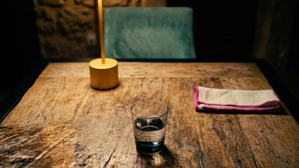 A still-life of an empty chair pushed back from a table and a glass of water, illustrating the Dua for Anger.