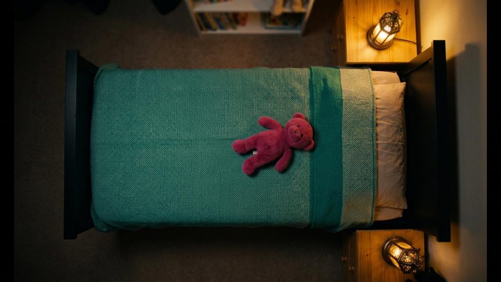 A still-life of a child's bed with a soft toy and a night lamp glowing beside it, illustrating the Dua for Children’s Protection.