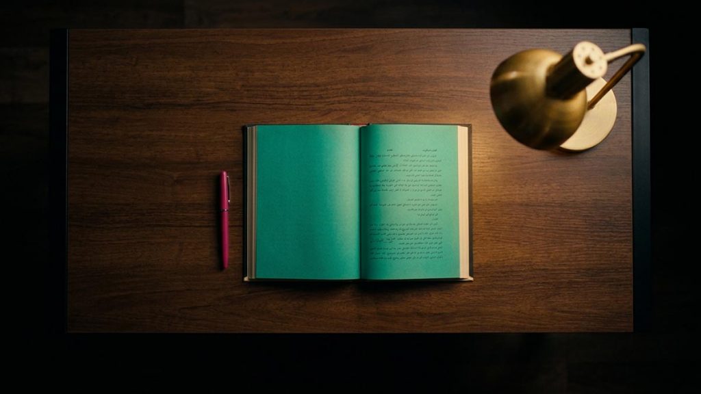A still-life of a bare desk with a single open book and a pen, illustrating the Dua for Concentration.