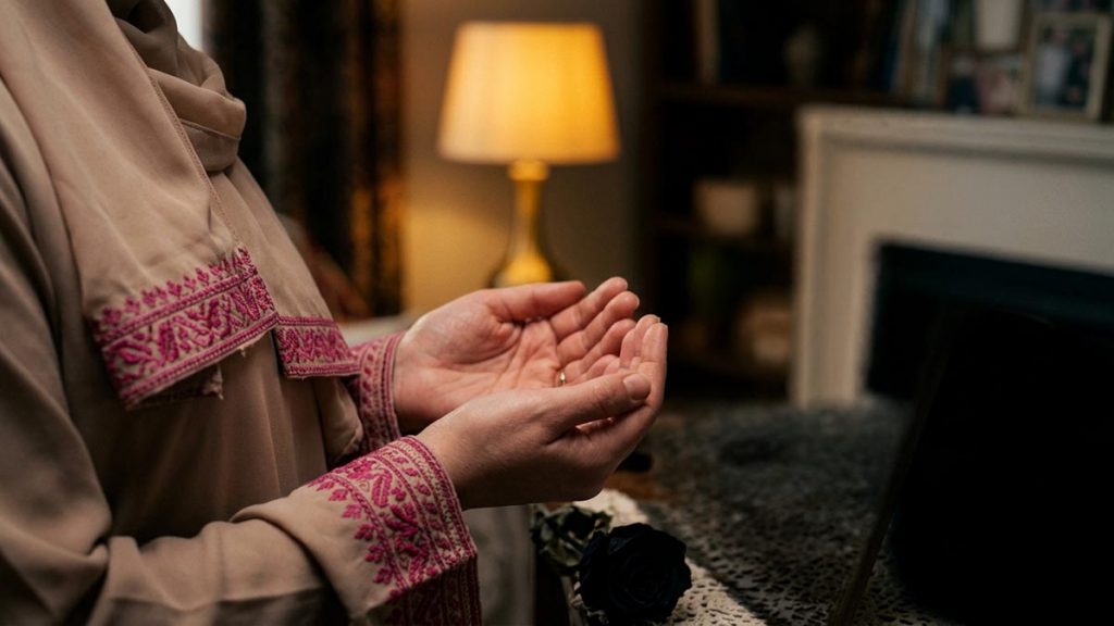 Close view of a Muslim woman's hands and the framed family photograph during the Dua for Deceased Relatives.