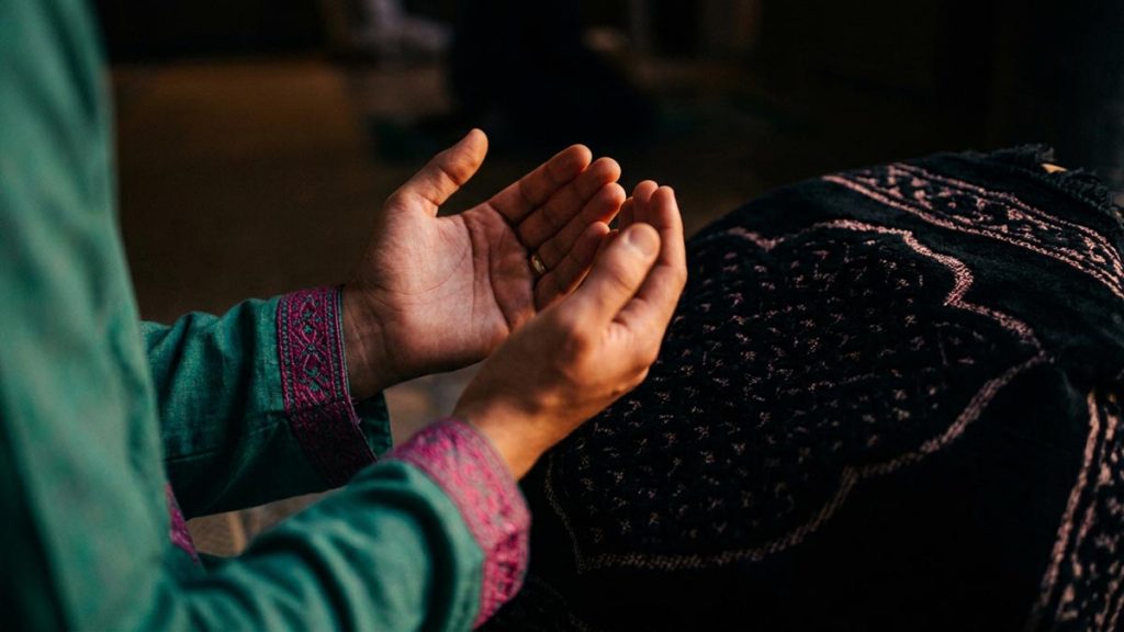 Close view of a Muslim man's hands and the prayer mat during the Dua for Leaving Sins.