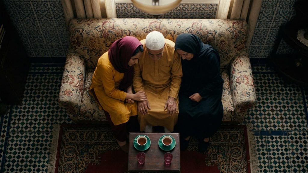 A Muslim family seen from behind in a sitting room where an adult child sits with elderly parents, reflecting the Dua for Parents.