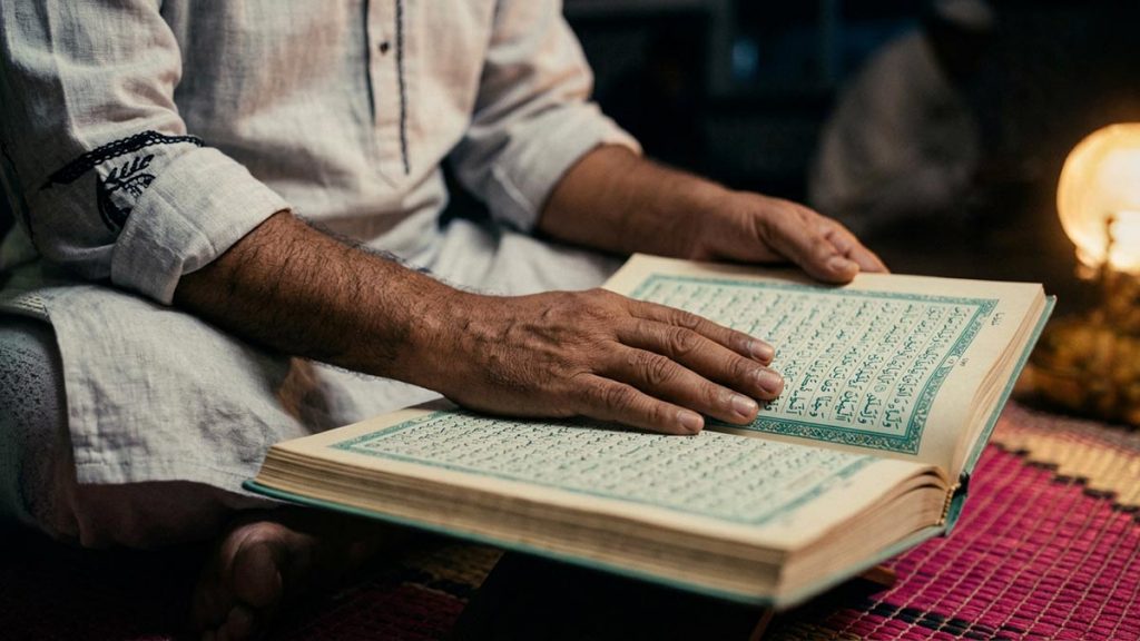 Close view of a Muslim man's hands and the open Quran and a prayer mat during the Dua for Qiyam al-Layl.