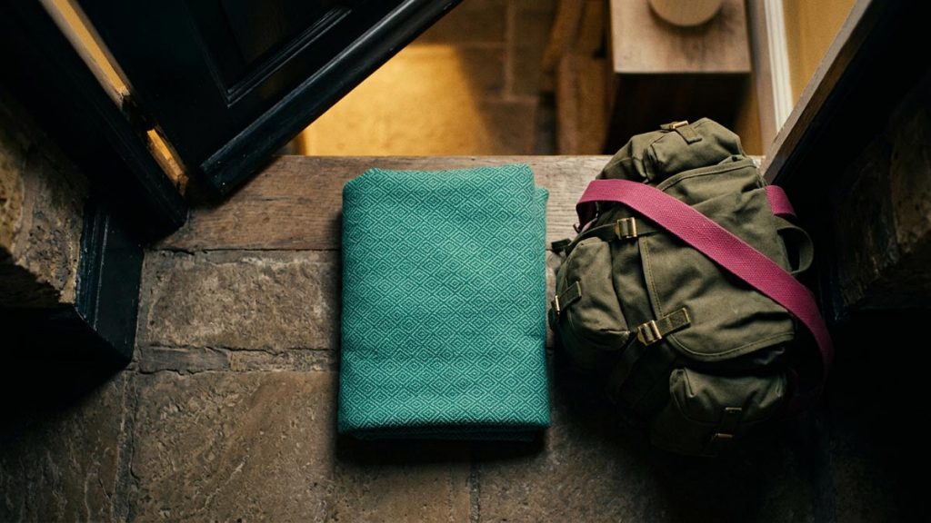 A still-life of a folded blanket and a packed emergency bag by a doorway, illustrating the Dua for Safety During Conflict.
