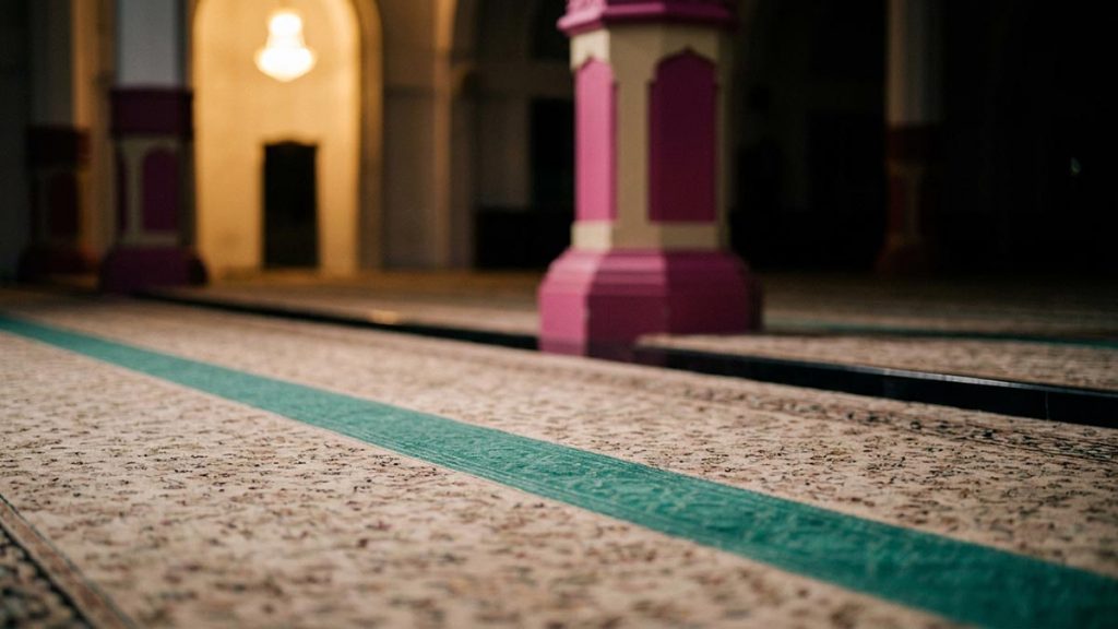 A still-life of a prayer hall with light falling steadily across the carpet, illustrating the Dua for Steadfastness.