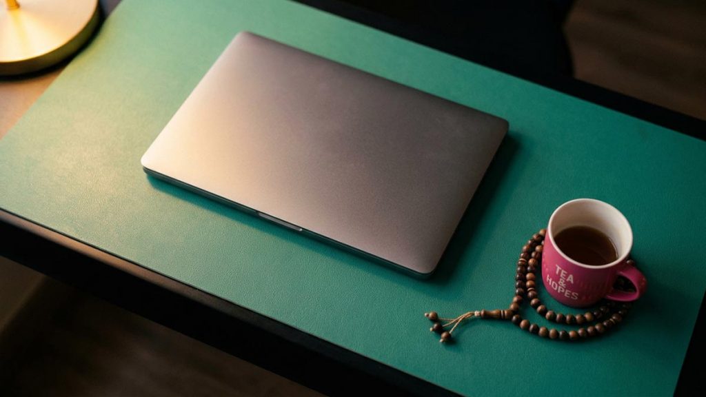 A still-life of a closed laptop, a cooling cup of tea and prayer beads on a desk, illustrating the Dua for Stress.