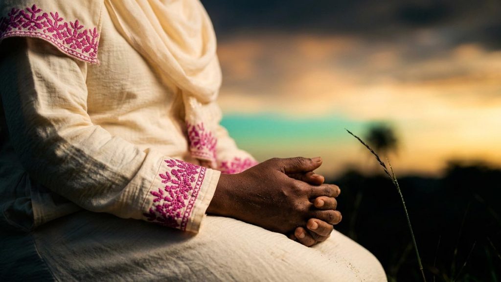 Close view of a Muslim woman's hands and the wide dawn sky during the Dua for the Day of Judgement.