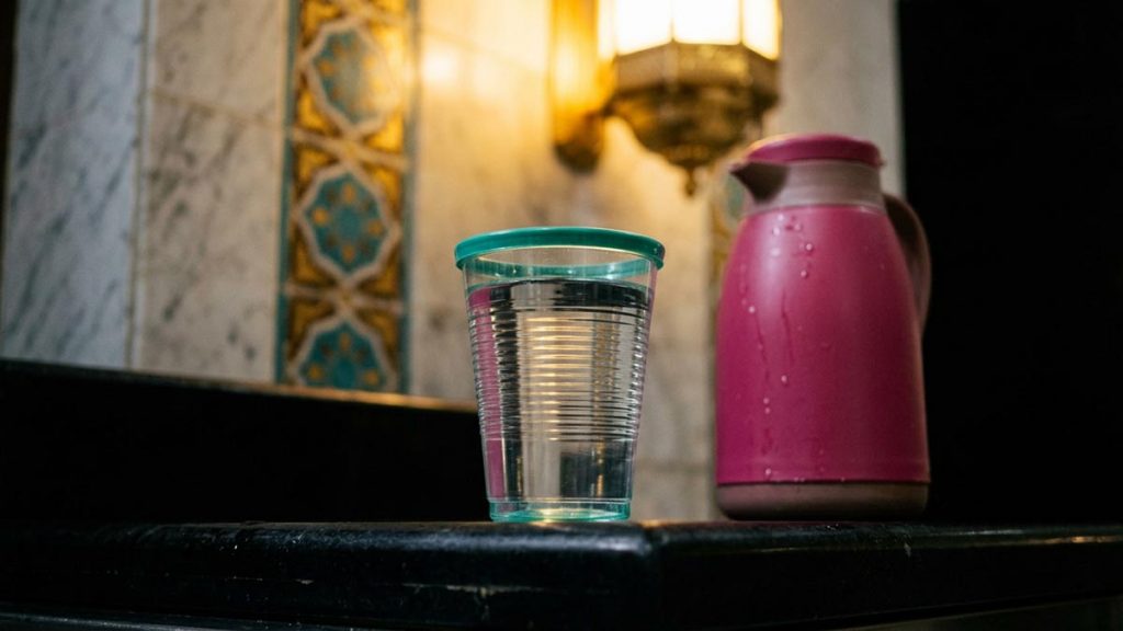 A still-life of a filled cup of blessed water beside a water flask, illustrating the Dua for Zamzam Water.