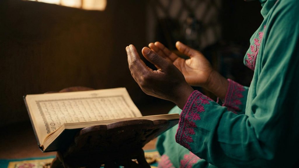 Close view of a Muslim woman's hands and the open Quran during the Dua of Prophet Adam.