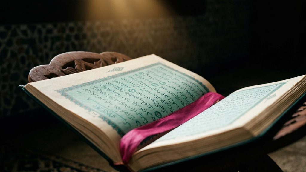 A still-life of an open Quran on a carved stand in a quiet mosque corner, illustrating the Dua of Prophet Ibrahim.