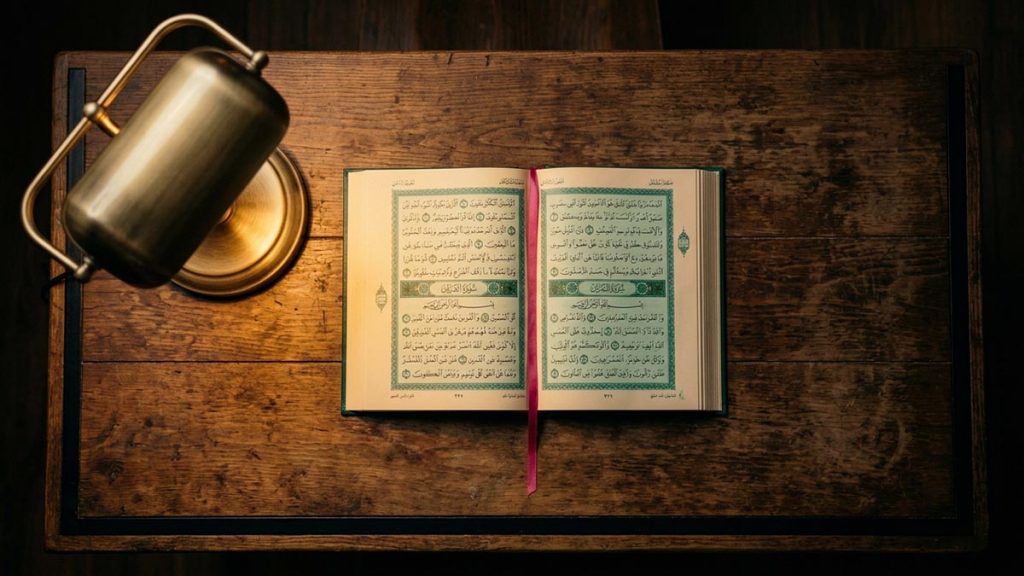 A still-life of an open Quran beside a lit lamp on a wooden desk, illustrating the Dua of Prophet Musa.