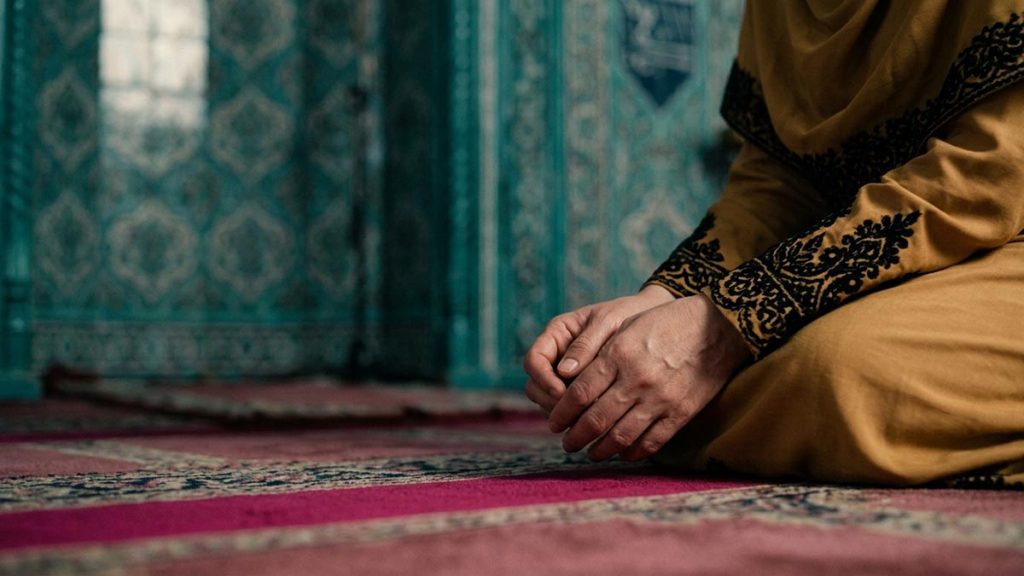 Close view of a Muslim woman's hands and the empty prayer niche during the Dua of Prophet Zakariyya.