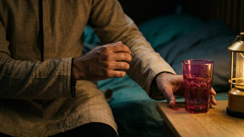 Close view of a Muslim man's hands and the glass of water and a small lamp during the Dua Upon Awakening from a Bad Dream.