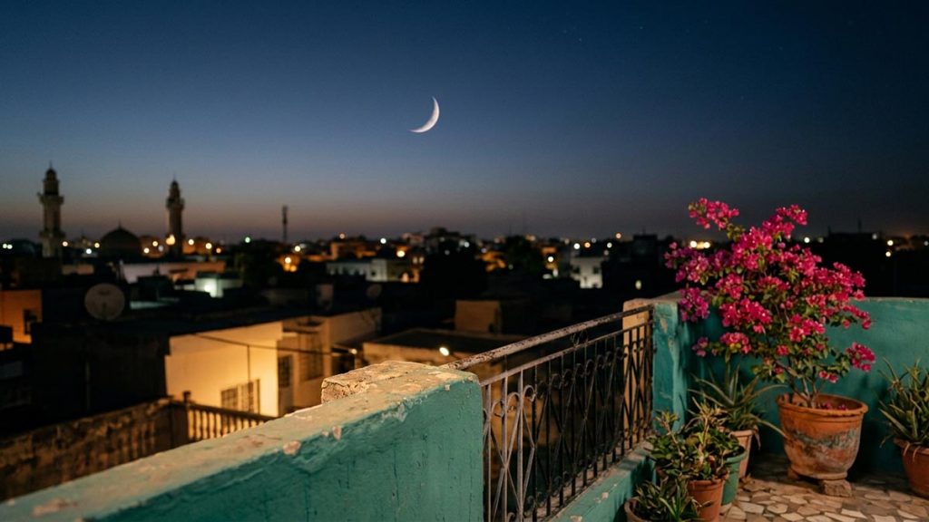 A still-life of a thin crescent moon above a rooftop parapet at dusk, illustrating the Dua Upon Seeing the New Moon.