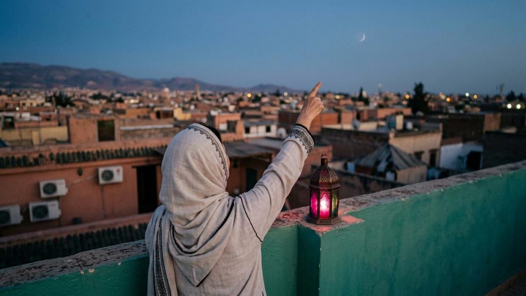A Muslim woman seen from behind on a rooftop watching for the crescent of the new month, reflecting the Dua Upon Sighting the Ramadan Moon.