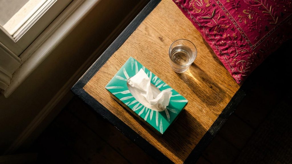 A still-life of a box of tissues and a glass of water on a side table, illustrating the Dua Upon Sneezing.