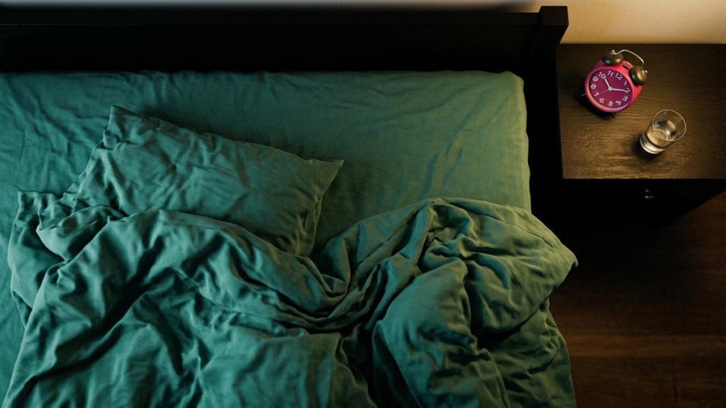 A still-life of rumpled bedding and a small clock on a bedside table in morning light, illustrating the Dua Upon Waking Up.