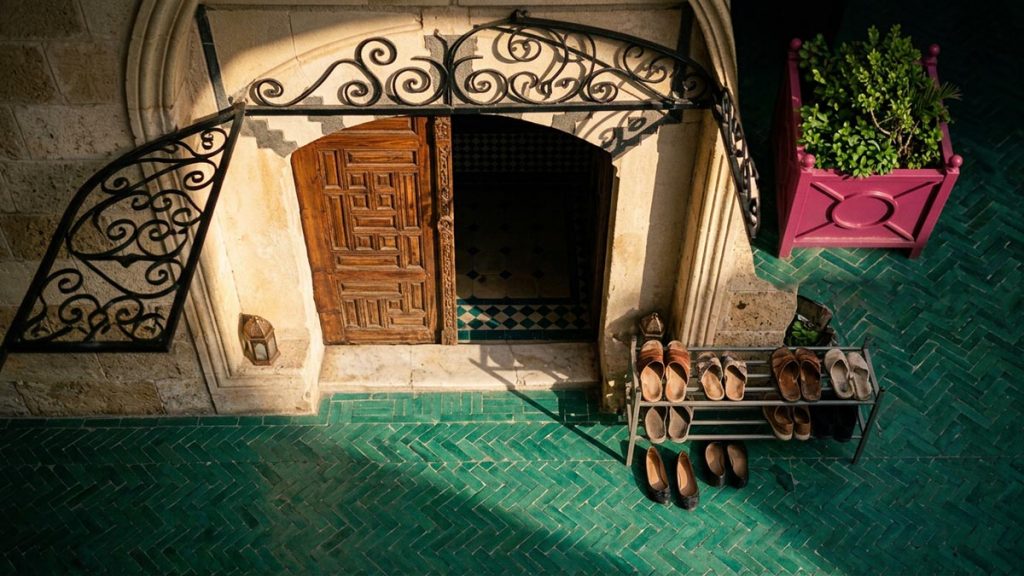 A still-life of an open mosque door with sunlight falling across the threshold and a shoe rack beside it, illustrating the Dua When Leaving the Mosque.