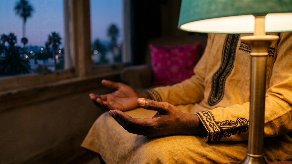 Close view of a Muslim man's hands and the lit table lamp during the Evening Dua.