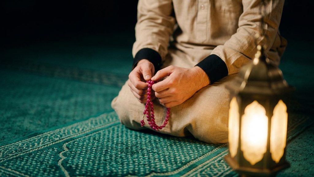 Close view of a Muslim man's hands and the prayer mat and a low lamp during the Qunoot al-Witr.