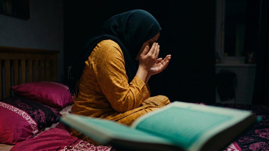 A Muslim woman seen from behind in a bedroom at night before sleep, reflecting the The Three Quls.