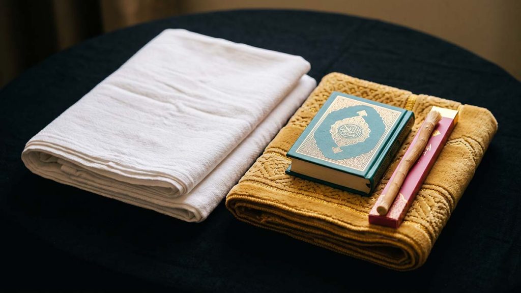 Hajj pilgrimage essentials including ihram garments, prayer mat and Quran