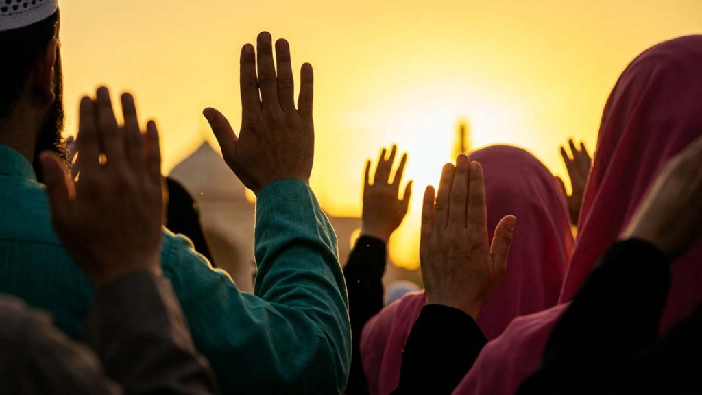 Muslim hands raised in the Takbir of Eid against a golden sunrise sky