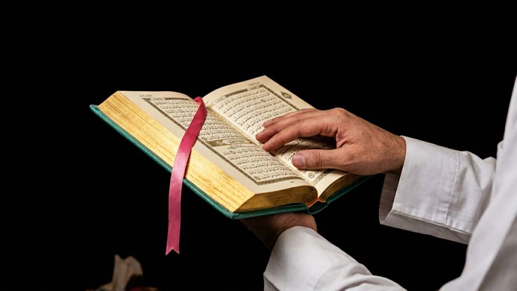 Muslim hands holding an open Quran during Taraweeh prayer in Ramadan