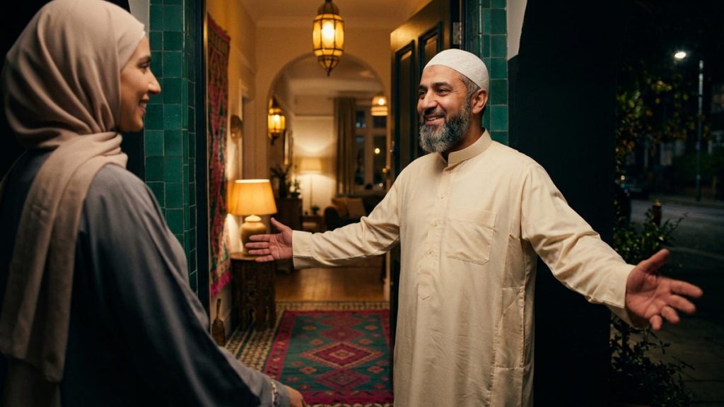 A smiling Muslim host welcoming a guest with open arms at the threshold of a warmly lit home, illustrating Ahlan wa Sahlan.
