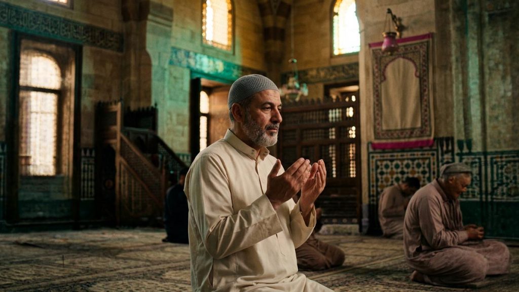 A worshipper sending blessings in quiet devotion, hands gently raised, in a softly lit mosque, evoking Sallallahu Alayhi wa Sallam.
