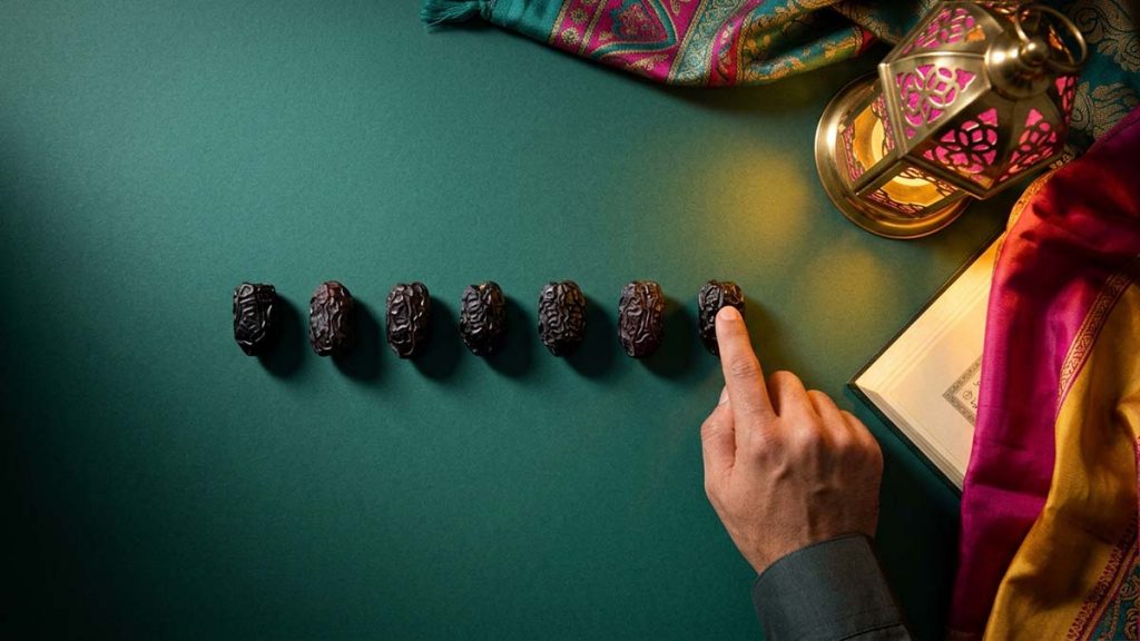 A hand counting seven Ajwa Dates beside an open book, evoking the hadith of seven dates