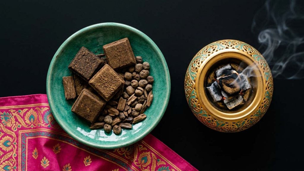 Assorted Bakhoor blocks in a teal dish beside a burner