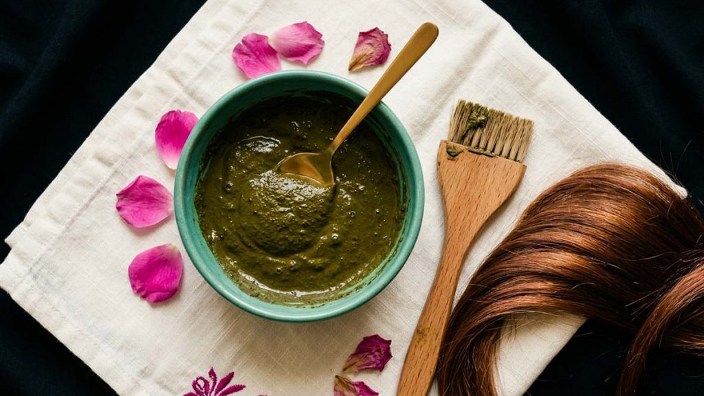 A bowl of Henna paste beside auburn-tinted hair, a natural hair dye