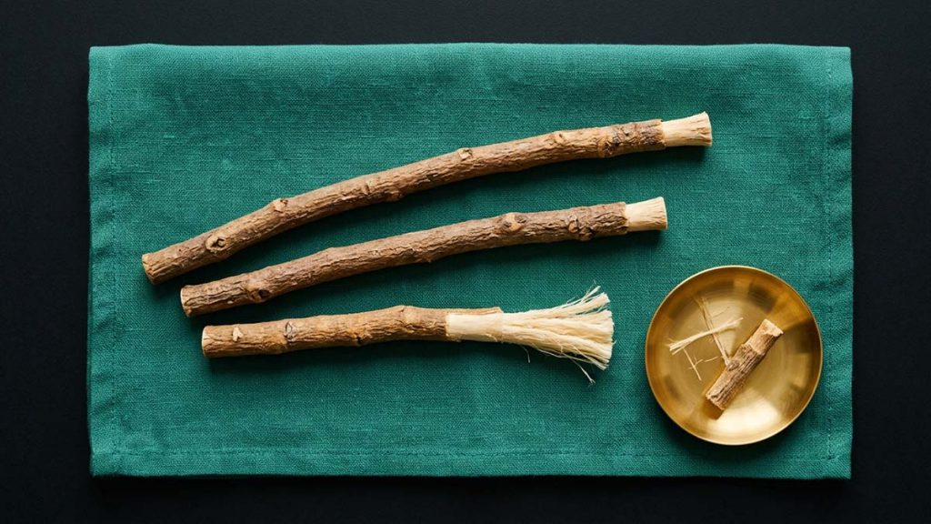 Three natural Miswak twigs fanned on teal linen, one peeled to show its cleaning fibres