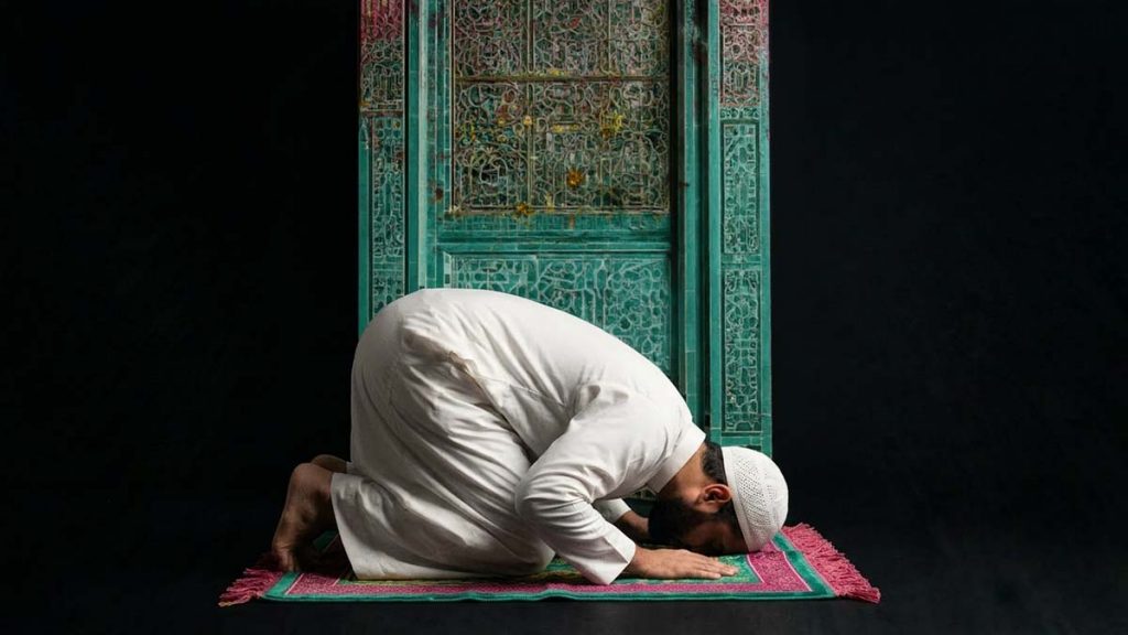 A Muslim man praying on a Prayer Mat before a teal-tiled niche